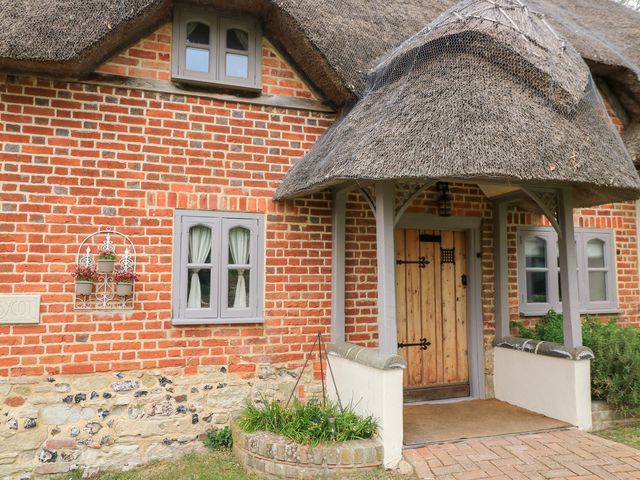 The front entrance of a brick and stone house with a thatched roof and wooden door at Cosy Cot in Stapleford