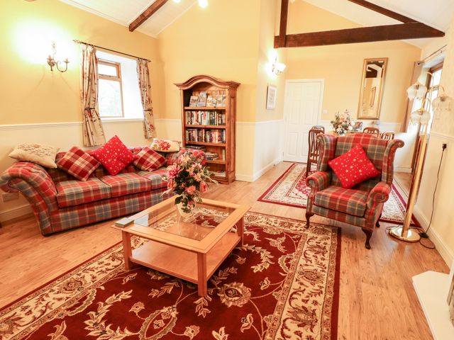 A living room with plaid sofa and armchair a wooden coffee table and bookshelf at The Barn in Snitterby