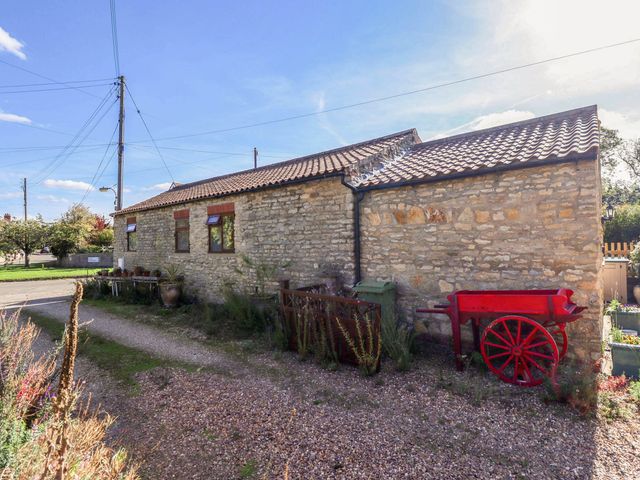 An outdoor view of a stone building with windows and a red wheelbarrow at The Barn in Snitterby