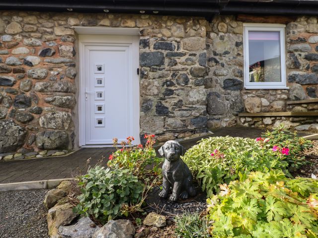 A stone building with a white door and window a garden bed with various plants and a dog statue at Bryn Eglwys Barn Llanegryn near Tywyn