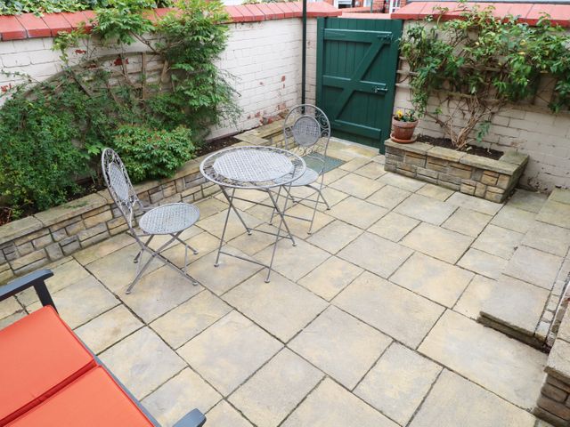 A small patio with metal table and two chairs stone planters along brick walls and a green gate at Sunlight Soap Cottage in Port Sunlight