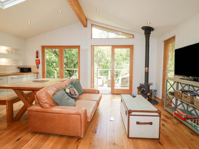 A living room with a leather sofa wooden table glass doors and a wood stove at 4 Stonerush Valley in Lanreath