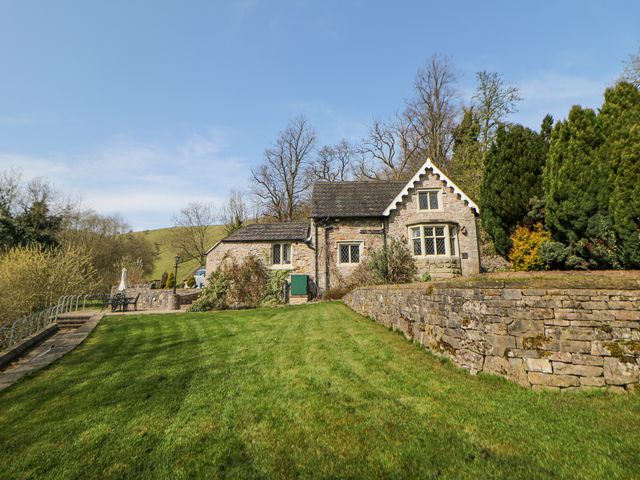 A stone cottage with a lawn and stone wall surrounded by trees at River Lodge in Ilam