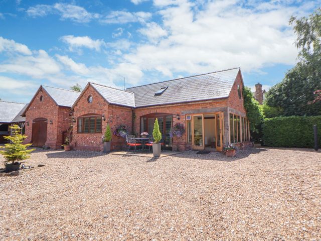 An outdoor area with a house and table on a gravel driveway at Honeysuckle Farmhouse in Tarporley