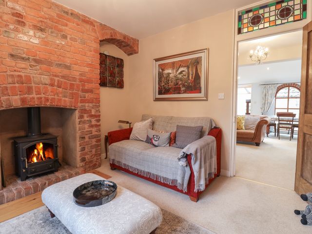 A living room with a red sofa covered with gray throws a brick fireplace with a wood burning stove and a patterned stool topped with a tray at Primrose Cottage in Kenton
