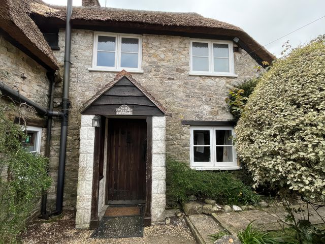 A stone cottage with a thatched roof and front door at Ivy Cottage in West Lulworth