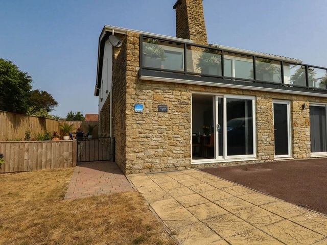 A house exterior with a balcony and stone wall at Tides Corner in Bowleaze