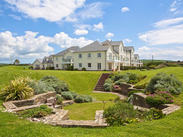 A large white multi-story building with balconies surrounded by green lawn and garden at 8 Thurlestone Beach in Thurlestone