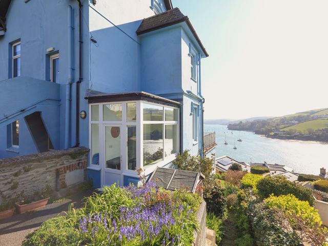 A blue house with a conservatory overlooking a river with boats and surrounding hills
