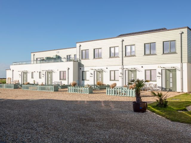 A row of white modern townhouses with green doors and small fenced gardens in front at 4 Ocean Reach in Bolberry