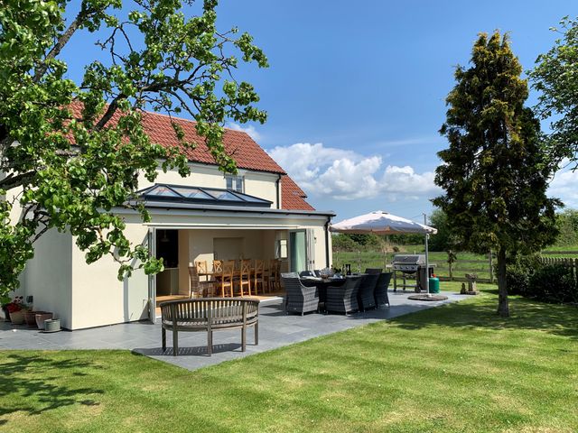An outdoor patio area with dining tables chairs umbrella barbecue and grassy lawn at The Retreat in Lympsham