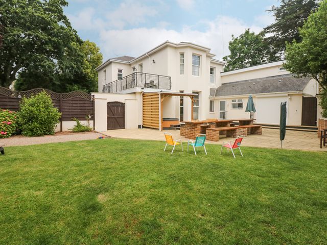 A backyard with a lawn and patio furniture including colorful chairs and a brick picnic table at Babbacombe Hall in Babbacombe