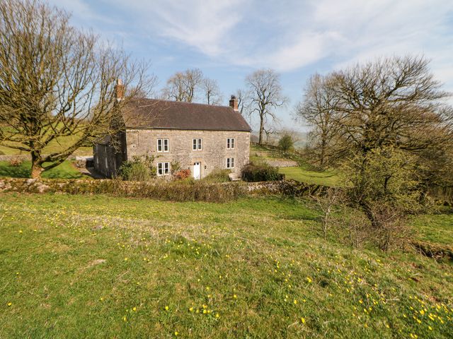 A stone house with multiple windows and a front door surrounded by grassy land and trees at Slade House in Ilam Staffordshire