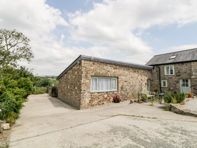A stone house with windows and doors surrounded by a concrete driveway and greenery at Owl Barn in Tavistock