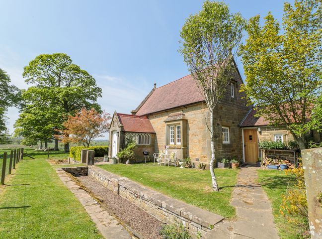 A stone cottage with a red tiled roof surrounded by green grass trees and a stone pathway at Fenwick Retreat at Fenwick Lodge in Fenwick near Ponteland