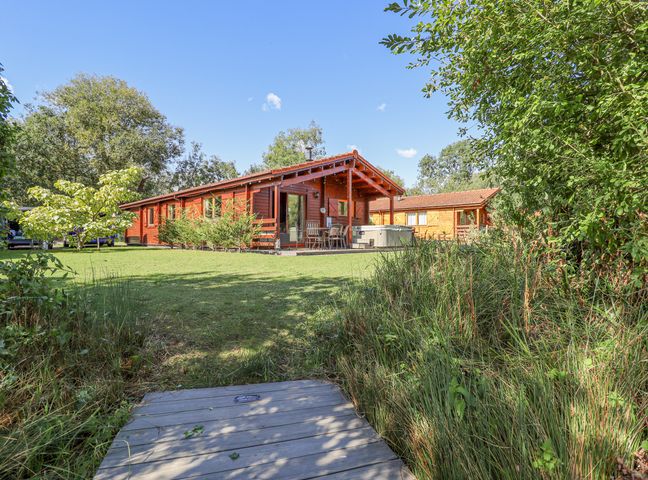 A wooden cabin with a covered patio and outdoor seating surrounded by grass and trees at Jemima Lodge in Tattershall