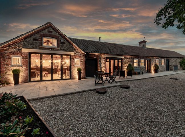 Exterior of a long stone building with large windows and outdoor seating at Sykes Lodge in Malton