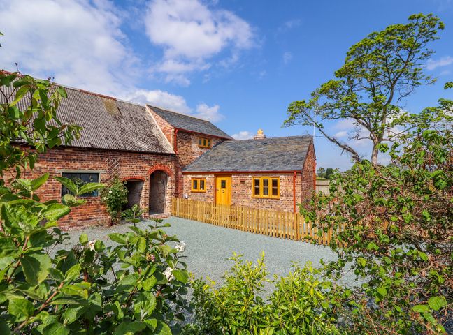 A brick house with a slate roof and wooden fence surrounded by plants and trees at The Tractor Shed in Kinnerley near Oswestry