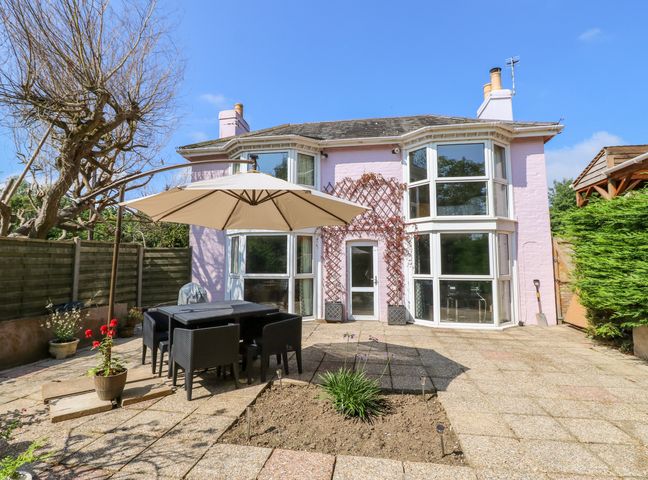 A backyard patio with outdoor dining set and umbrella next to a house with large windows at St Michaels House in St Helens