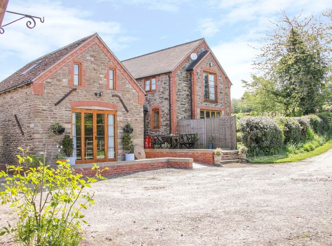 A stone brick house with wooden framed windows and a gravel driveway at High Grove in Ludlow