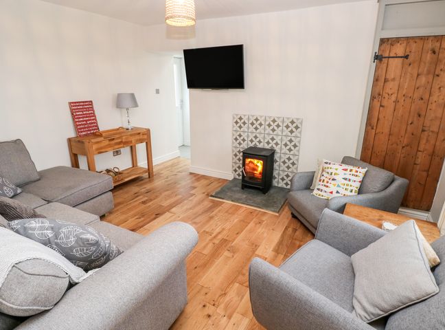 A living room with grey sofas a wood stove under a mounted TV and a wooden console table at Coeden Bach in Burry Port