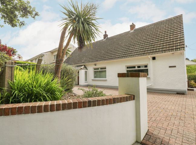 A white house with a tiled roof and paved driveway with plants and a small wall at Ashdown House in Saundersfoot