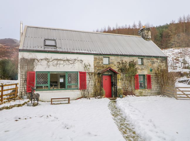 A house with red shutters and a red door surrounded by snow at The Old Mill in Cannich