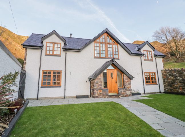 A two story house with multiple windows and a wooden front door with stone around it and a grass lawn in front at Bwthyn Carregwen in Dwygyfylchi