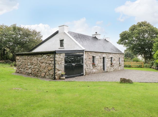 A stone cottage with a slate roof and green grass surrounding it at An Teach Ban in Rossaveel County Galway