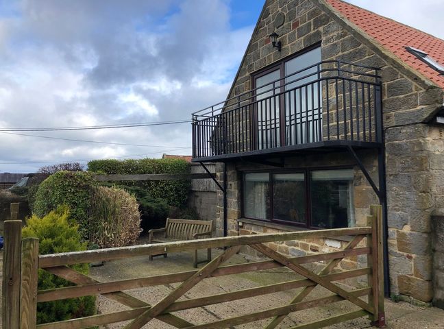 A stone house with a balcony and a wooden gate in front at Mill House in Robin Hood's Bay