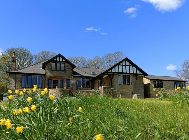 A stone house with black framed windows and daffodils in the foreground at Castleys in Skipton