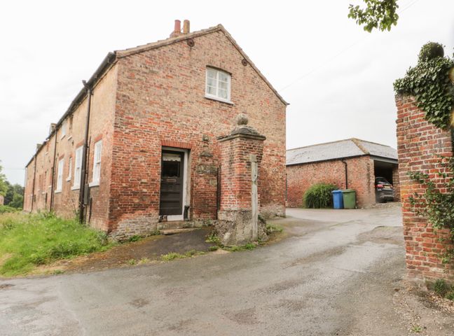 A brick house with a black door and white windows beside a driveway leading to a garage with two trash bins at Bellas Cottage in Driffield
