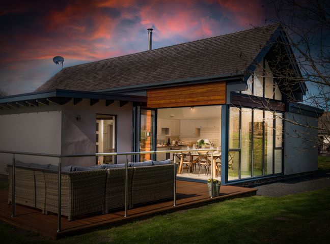 A house with an outdoor seating area and a kitchen visible through large glass doors at Lambs Lodge in Bamburgh