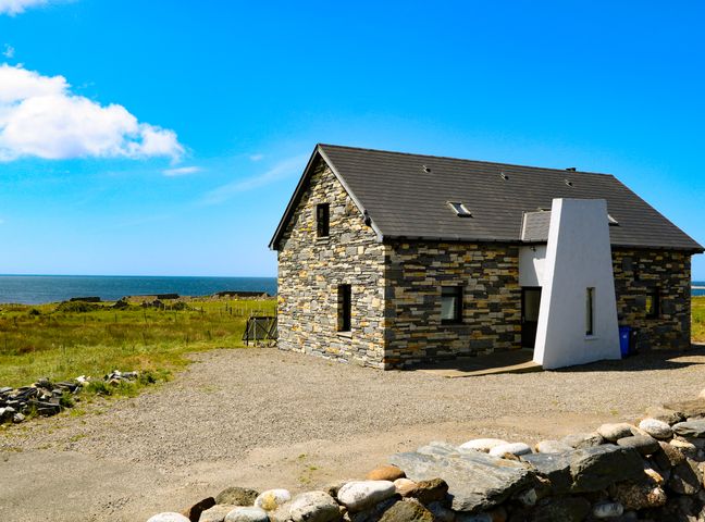 A stone house with a sloped roof near a grassy field and the sea at Ocean Sail House in Termon near Dungloe County Donegal