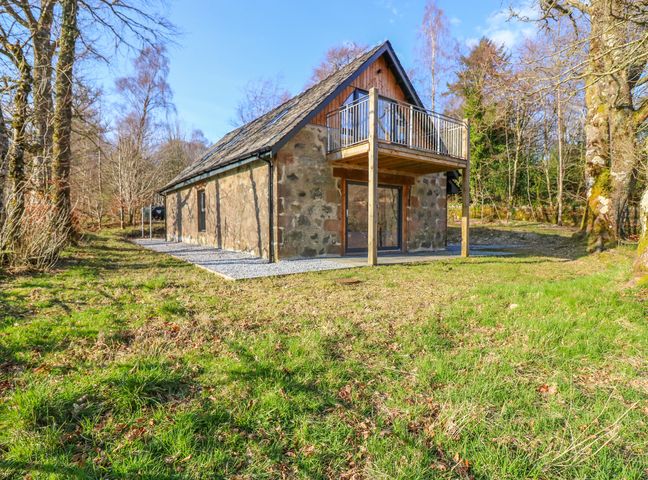 A stone house with a balcony surrounded by grass and trees at Boat House in Invergarry