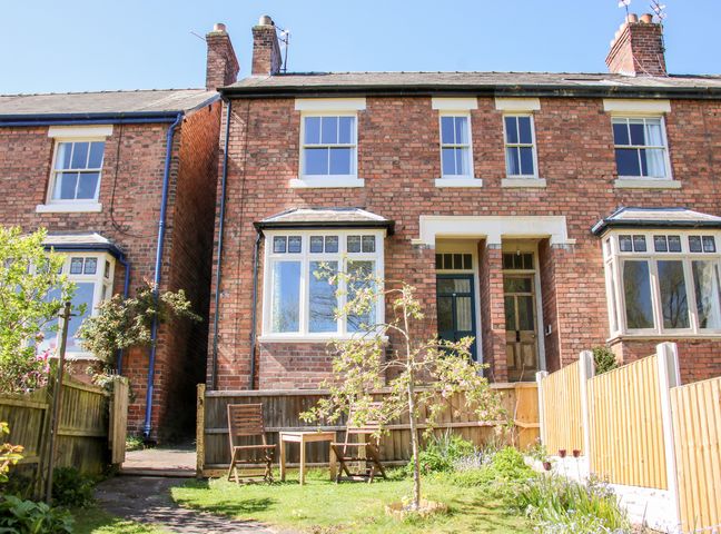 A backyard garden with a small tree two wooden chairs and a table in front of a brick house at Willow View in Shrewsbury