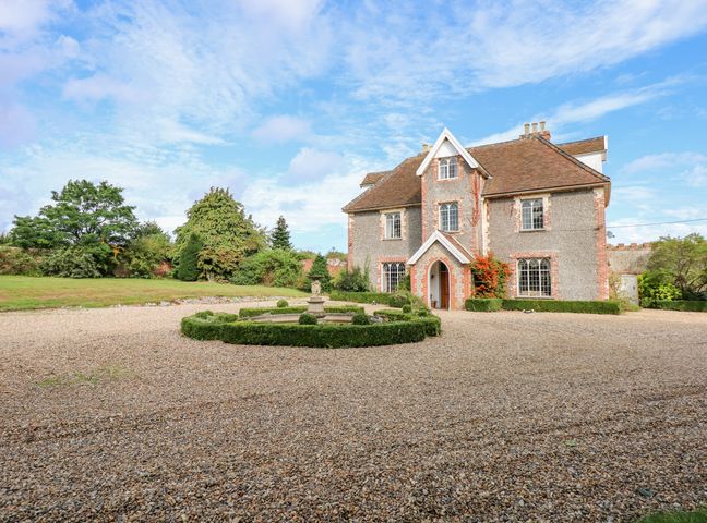 A large stone house with a circular hedge and fountain in front in a gravel driveway at Southrepps Lodge in Southrepps