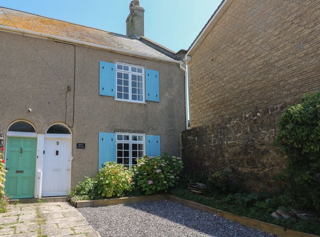 An exterior view of a cottage with blue window shutters a white door and a small garden area at Brock Cottage in West Bay