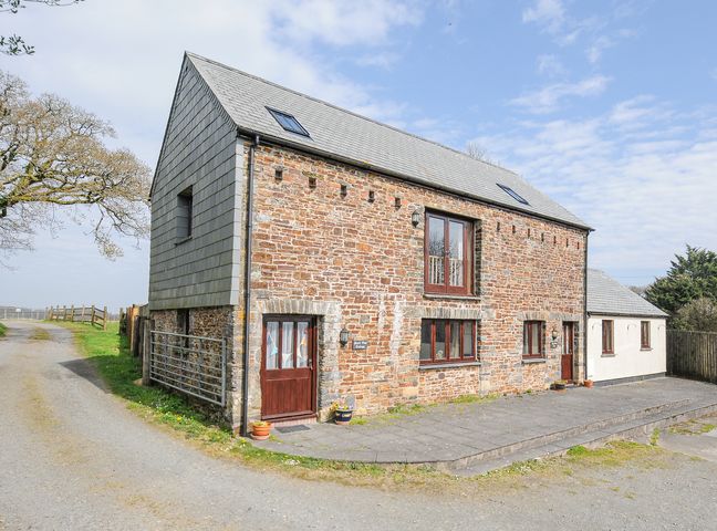Exterior view of a stone and brick house with multiple windows and a paved area at Barn Owl Cottage Canworthy Water near Launceston