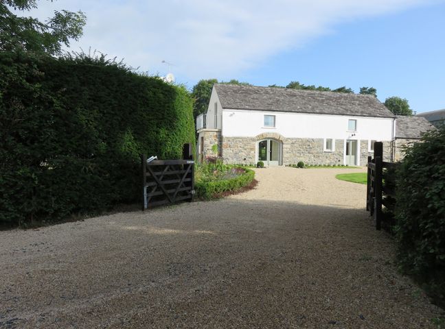 A gravel driveway leading to a stone and white house with a wooden gate and tall hedges at Old Village Barn Woodford County Galway