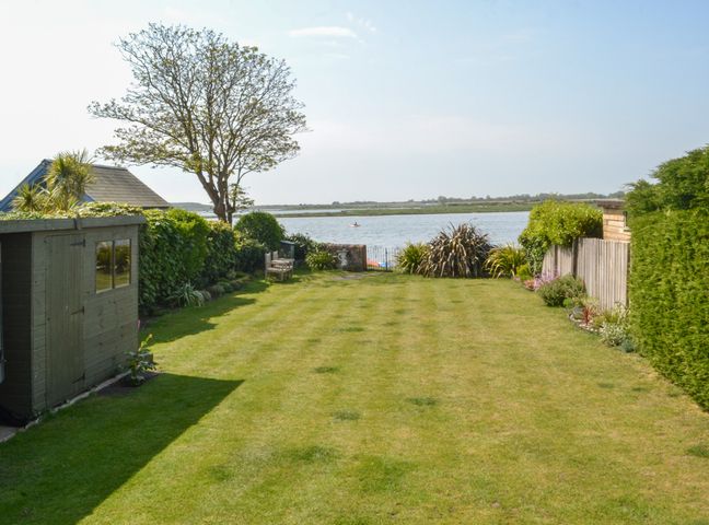 A garden with a shed and a bench overlooking a body of water at Harbour View Mudeford in Christchurch