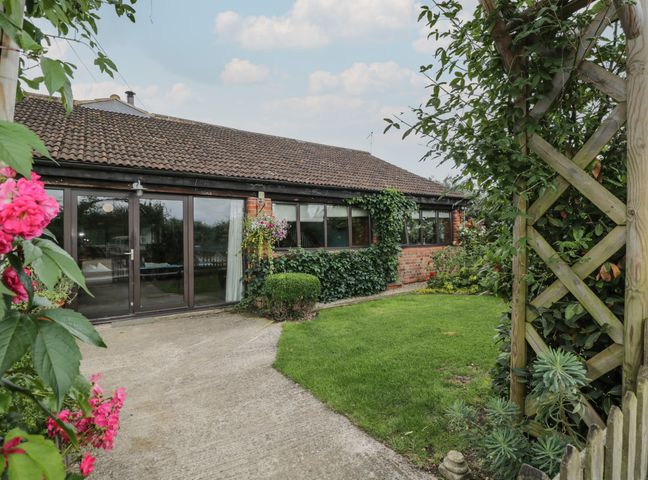 A garden area with grass and flowers and a wooden trellis at The Barn in Draycot Cerne near Malmesbury