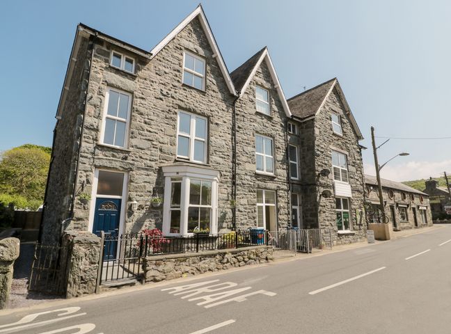 A stone building with multiple windows and blue doors along a street at Angorfa in Llanbedr