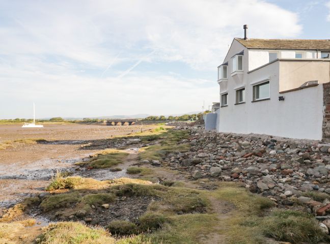A rocky shoreline with a white building on the right and a sailboat on the left at Waterside in Ravenglass