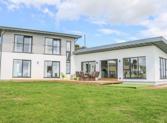 A modern two-story house with large windows and a wooden deck with outdoor dining furniture at Beach House Courtown County Wexford