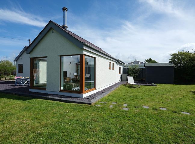 A white house with large corner windows a lawn and a garden chair at Awelon in Botwnnog