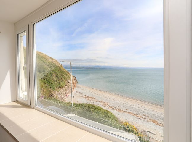 A large window with a view of a rocky beach and sea at Captains Rest in Criccieth