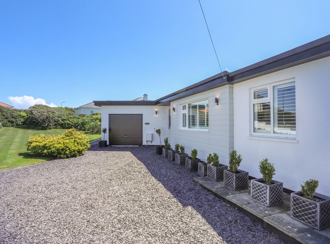 A driveway with potted plants leading to a garage attached to a white house with windows at Gadlys in Trearddur Bay