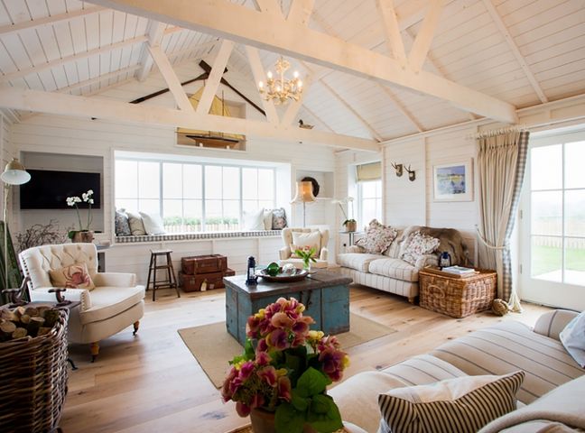 A living room with armchairs sofas a coffee table and large windows at Lligwy Beach Cottage in Moelfre