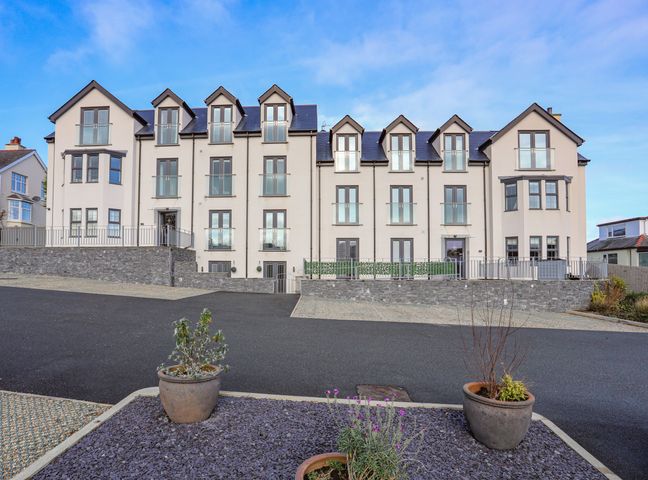 A large white multi-story residential building with multiple windows and balconies outside plants in pots at The Pot Loft in Benllech